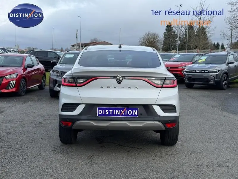Vue arrière d'un Renault Arkana blanc 2025 avec feux reliés par un bandeau lumineux rouge, sur un parking extérieur.