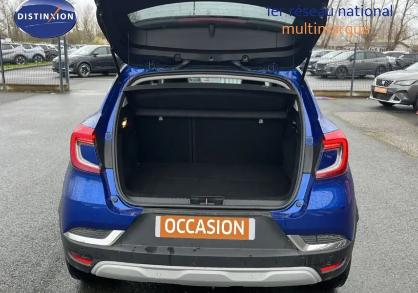 Vue arrière du Renault Captur bleu Iron Metal avec coffre ouvert, toit noir visible, sur parking extérieur.