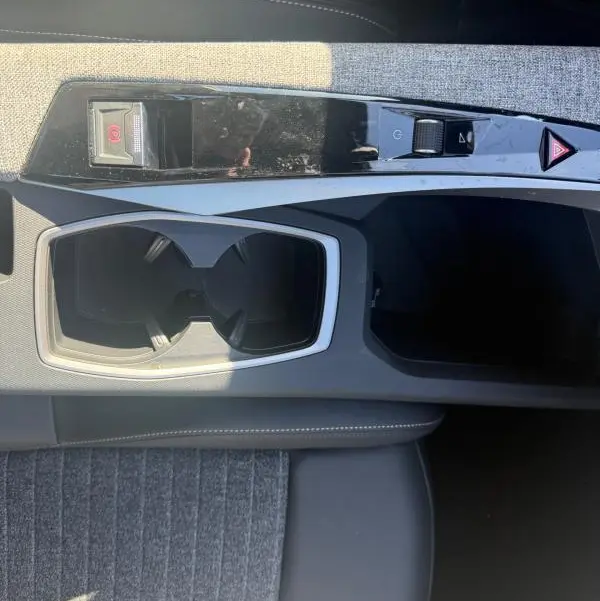 Vue plongeante sur la console centrale grise du Peugeot 3008 Hybrid 145, avec porte-gobelets et commandes de frein à main électrique.