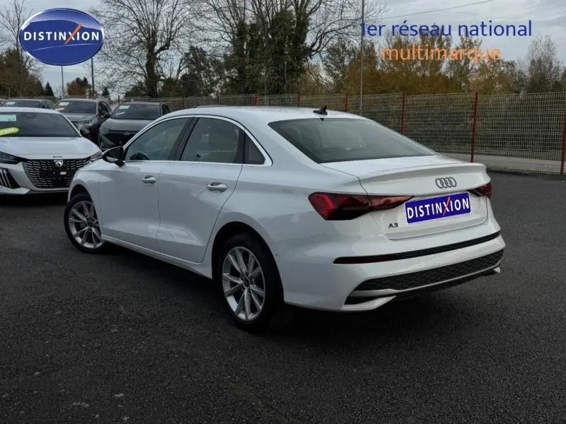 Audi A3 Sportback blanche vue 3/4 arrière droit, avec becquet et jantes alu sur parking extérieur.