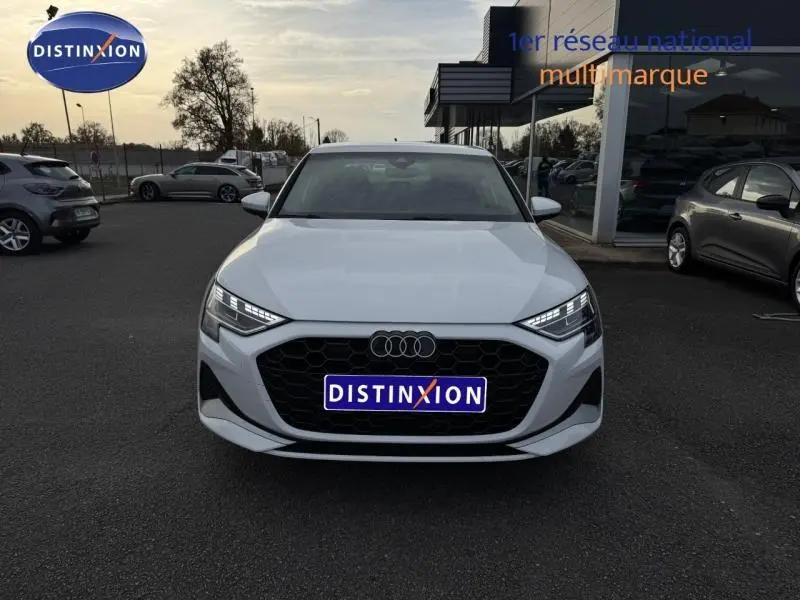 Audi A3 Sportback blanc vue de face avec calandre noire et phares LED allumés sur parking extérieur.