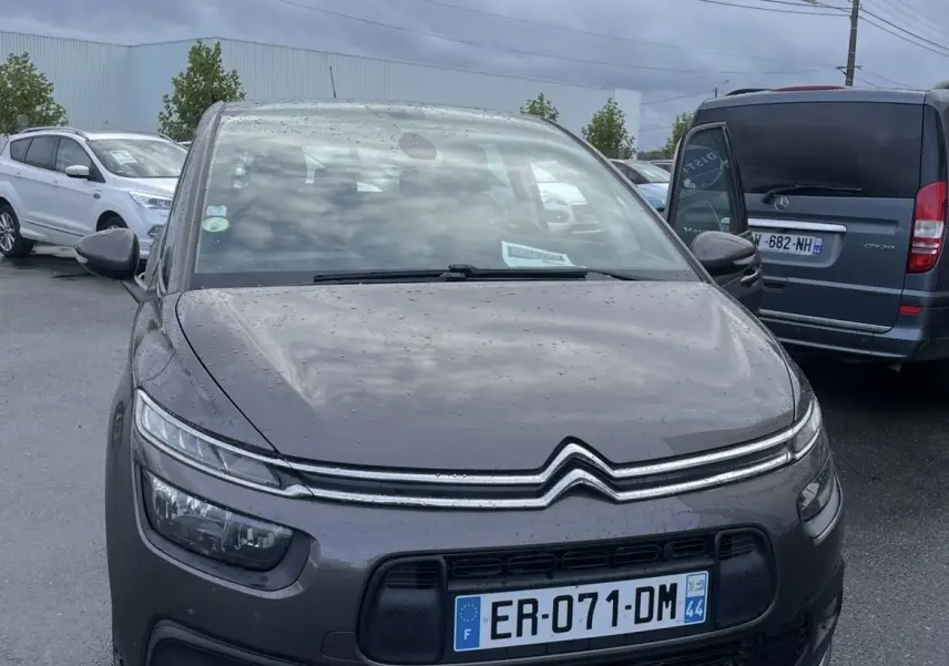 Citroën C4 Picasso marron vue de face sous la pluie, avec feux de jour LED et calandre distinctive.
