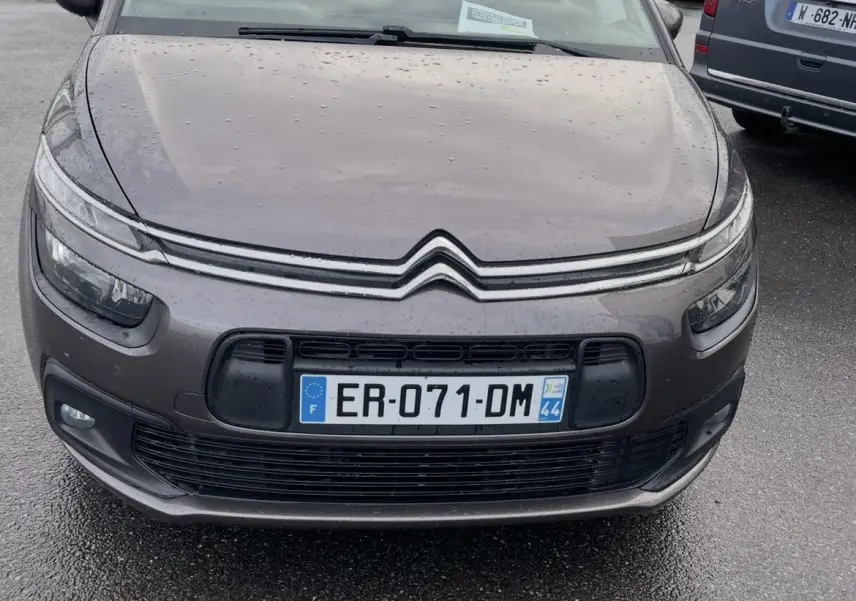 Vue avant d'une Citroën C4 Picasso marron 2017 avec pluie sur la carrosserie et plaques françaises visibles.