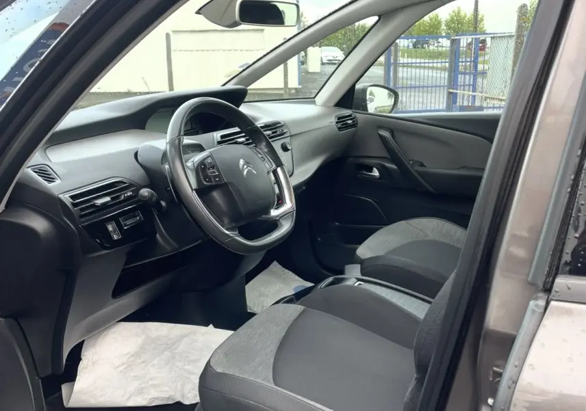 Vue intérieure côté conducteur du Citroën C4 Picasso marron 2017, volant cuir multifonction et sièges gris bi-ton.