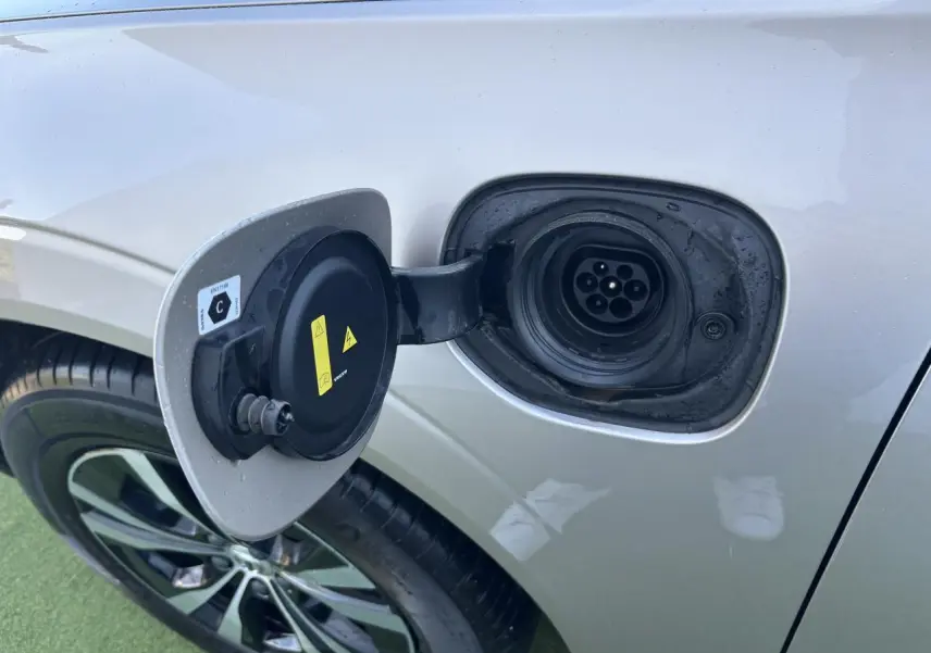 Prise de recharge ouverte côté gauche d'un Volvo XC60 argent crépuscule métallisé, jante alliage visible.