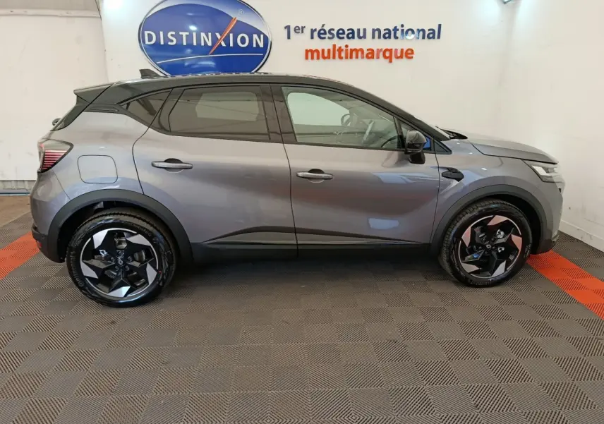 Profil droit du Renault Captur gris foncé 2025 avec jantes noires et toit noir dans un showroom intérieur.