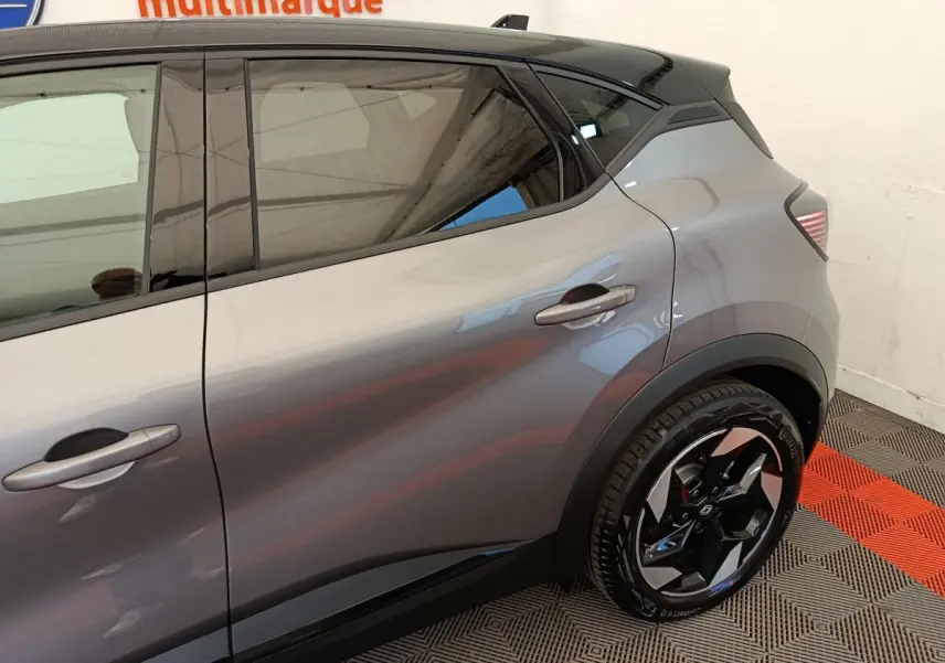 Vue côté droit arrière d'un Renault Captur gris foncé avec jante noire et toit noir dans un showroom.