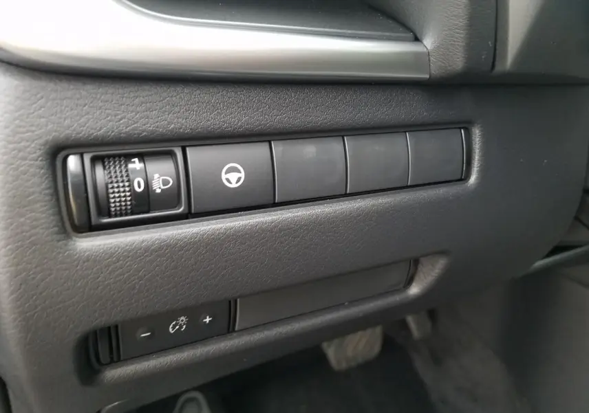 Gros plan sur les commandes de réglage des phares et assistance au volant du Nissan Qashqai noir, côté conducteur.
