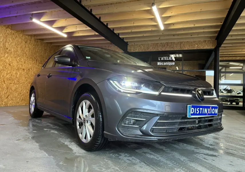 Volkswagen Polo gris 1.0 TSI 95 STYLE vue 3/4 avant avec projecteurs allumés en intérieur d'atelier.