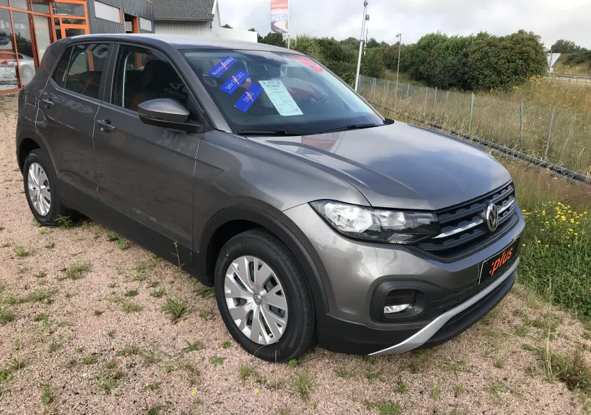 Volkswagen T-Cross gris limestone en vue 3/4 avant droit, avec jantes alliage et calandre noire distinctive.