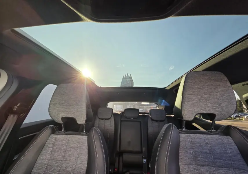 Vue intérieure arrière du Renault Austral 2025 avec sièges gris et toit panoramique en verre laissant passer la lumière du soleil.