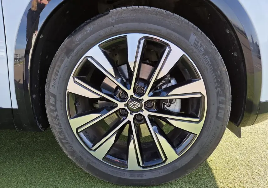 Gros plan sur la jante alliage 19 pouces Komah diamantée noire du Renault Austral blanc nacré avec toit noir.