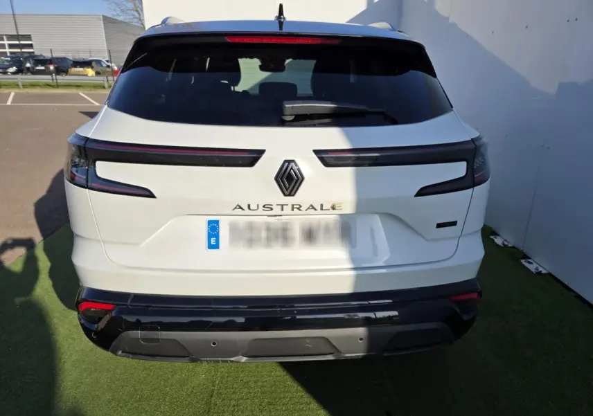 Vue arrière d'un Renault Austral blanc nacré avec toit noir, feux arrière LED et logo centré sur un parking.