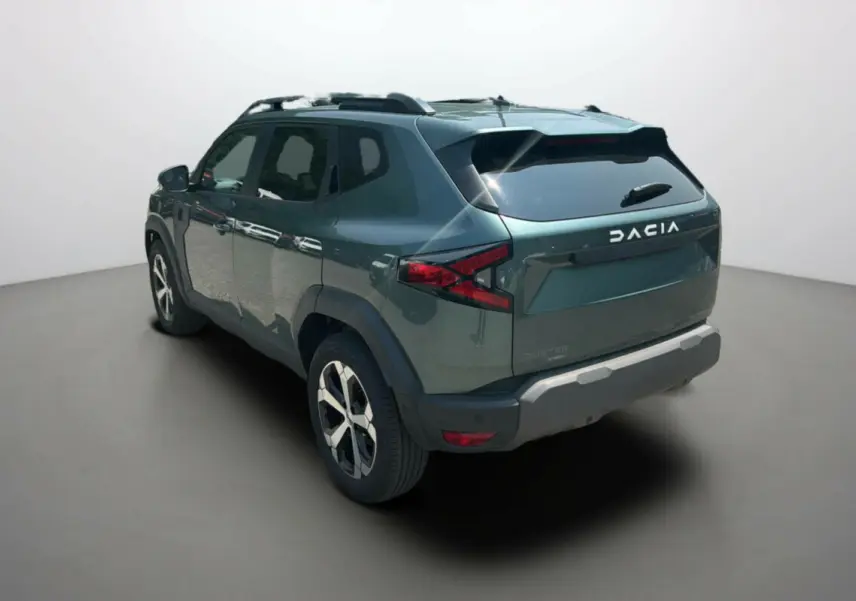 Vue 3/4 arrière droite du Dacia Duster 2025 vert cèdre avec jantes alu 18 pouces et barres de toit visibles.