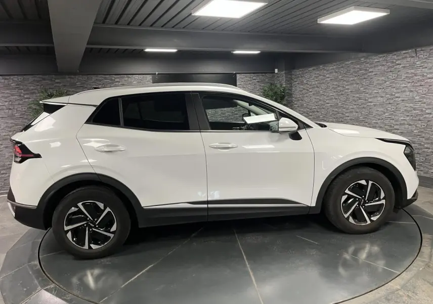 Profil côté gauche d'un KIA SPORTAGE blanc nacré 2022 avec jantes alliage 18 pouces et vitres surteintées.