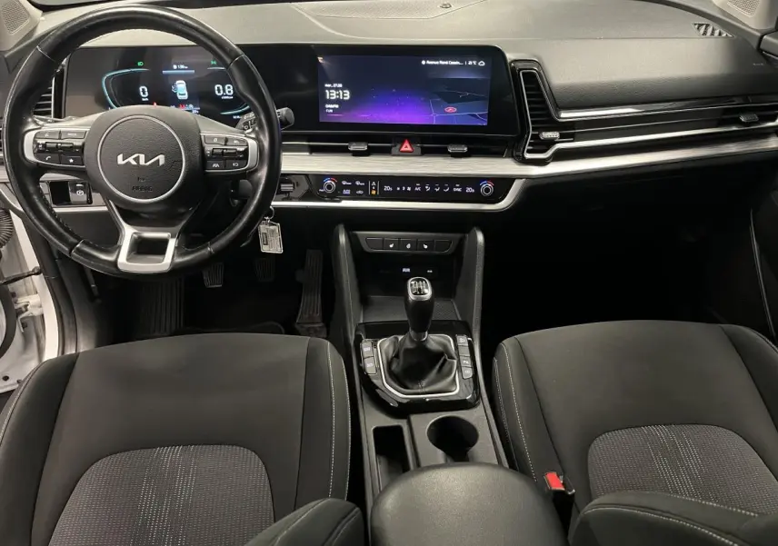 Intérieur du Kia Sportage 2022 vue avant, tableau de bord noir avec écran tactile et levier de vitesses manuel.