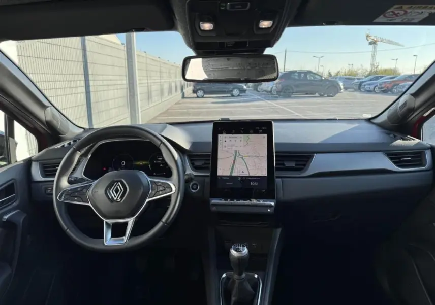 Vue intérieure avant du Renault Captur II rouge flamme, montrant le volant, écran tactile vertical et levier de vitesse manuel.