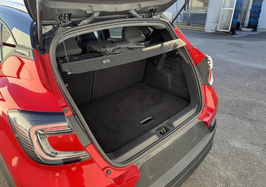 Coffre ouvert en vue arrière d’un Renault Captur II rouge flamme avec toit noir, montrant l’espace de chargement vide.