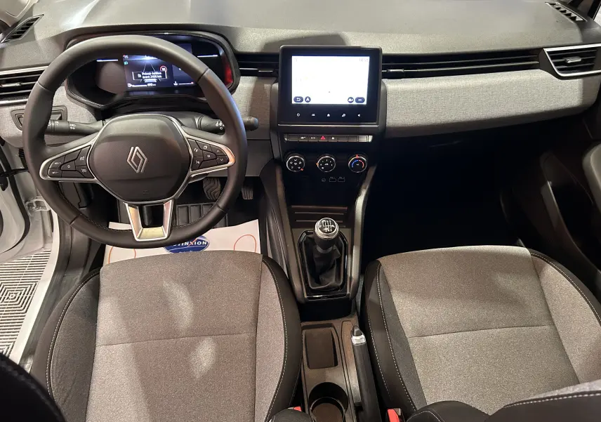 Vue intérieure frontale du poste de conduite de la Renault Clio V blanche avec volant multifonction et boîte manuelle.