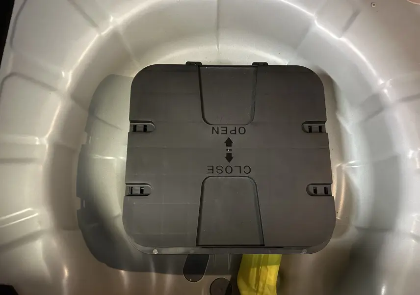 Vue plongeante sur le coffre blanc d'une Renault Clio V, mettant en valeur un compartiment noir avec indications d'ouverture.