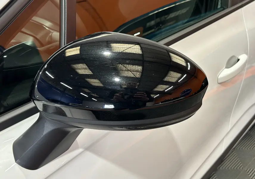 Gros plan sur le rétroviseur noir côté gauche d’une Renault Clio V blanche, vue partielle de la porte avant.