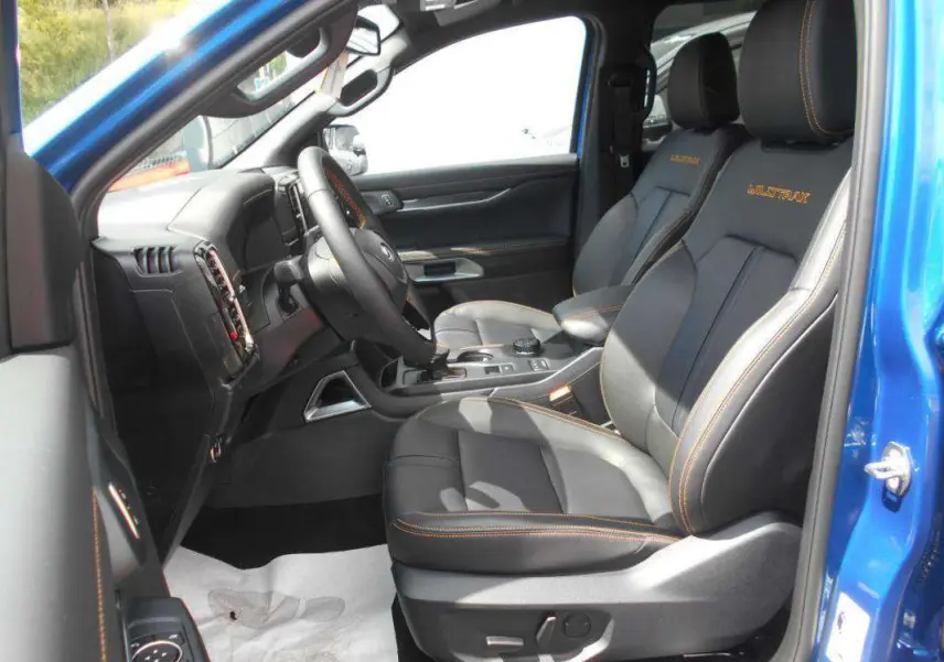 Intérieur du Ford Ranger 2025 bleu lightning vu côté gauche, sièges cuir noirs avec surpiqûres orange et logo Wildtrak.