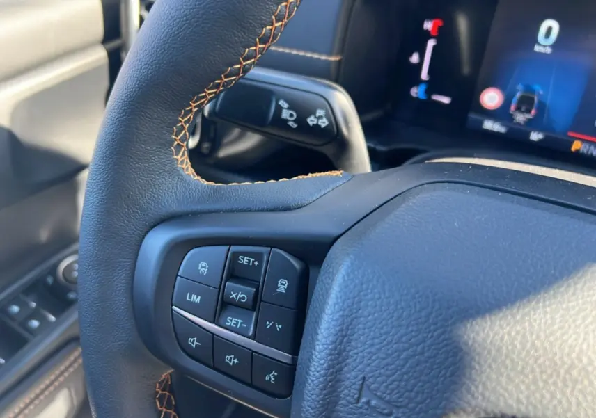 Gros plan sur le volant du Ford Ranger 2025, version Wildtrak Plus, avec commandes intégrées et coutures orange visibles.