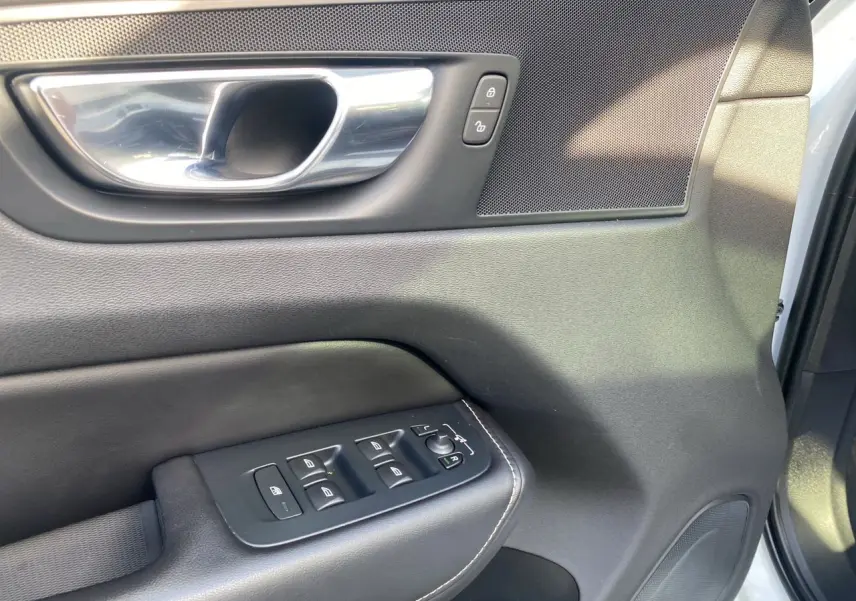 Gros plan sur la porte avant gauche du Volvo XC60 blanc 2019, montrant les commandes de vitres et la poignée intérieure chromée.