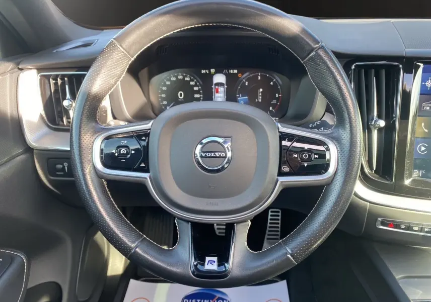 Vue rapprochée du volant cuir noir perforé du Volvo XC60 D4 2019 avec tableau de bord numérique et console centrale visible.