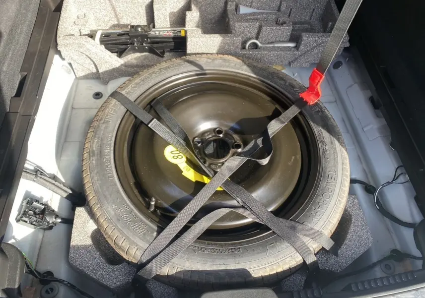 Roue de secours noire attachée par des sangles dans le coffre d'un Volvo XC60 blanc 2019, vue de dessus.