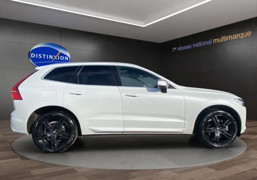 Vue latérale droite du Volvo XC60 blanc 2019 R-Design avec jantes noires et vitres teintées en showroom.