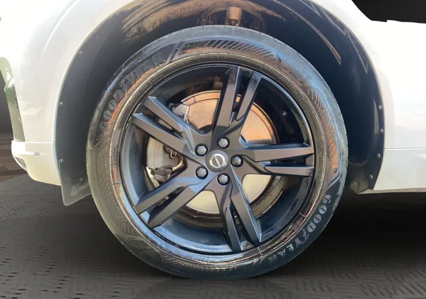 Gros plan sur la roue avant droite noire à jante alliage du Volvo XC60 blanc, version D4 R-Design 2019.