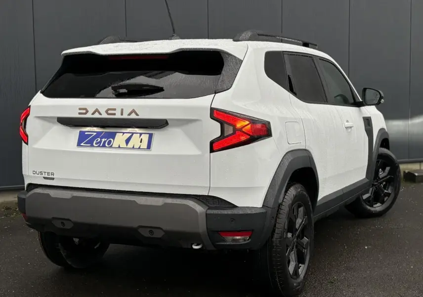Vue 3/4 arrière droite du Dacia Duster blanc Glacier avec jantes noires et barres de toit noires.