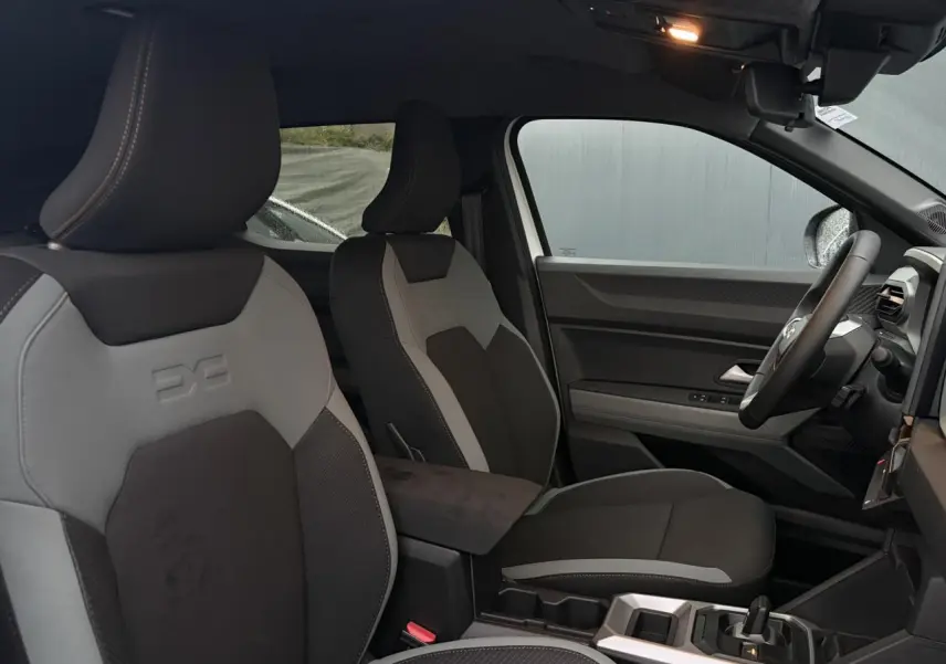 Vue intérieure côté droit du Dacia Duster 2026 Hybrid blanc Glacier, montrant les sièges bicolores et la console centrale moderne.