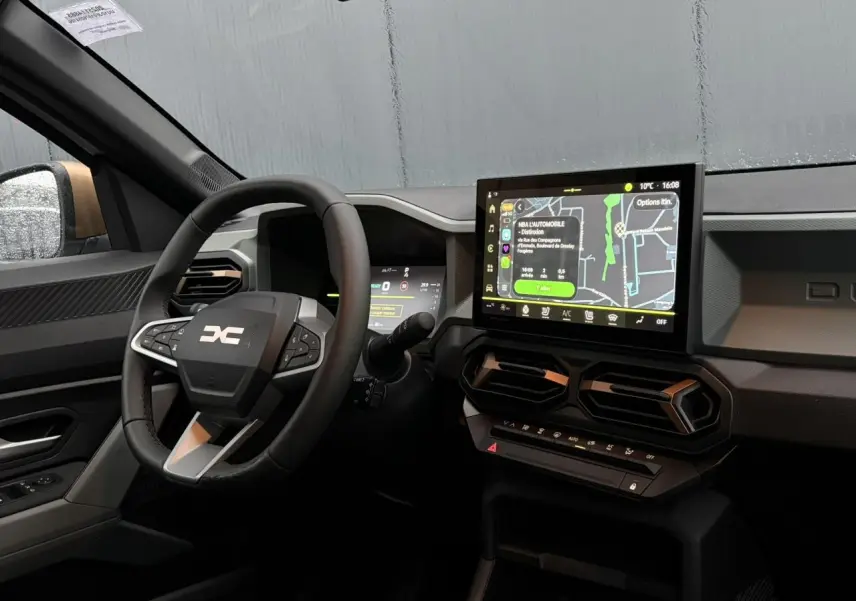 Vue intérieure côté conducteur du Dacia Duster 2026 avec volant noir, écran tactile central et détails brun cuivré.