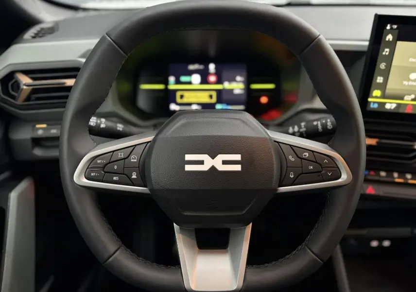 Vue rapprochée du volant noir du Dacia Duster 2026 avec commandes intégrées et tableau de bord digital en arrière-plan.