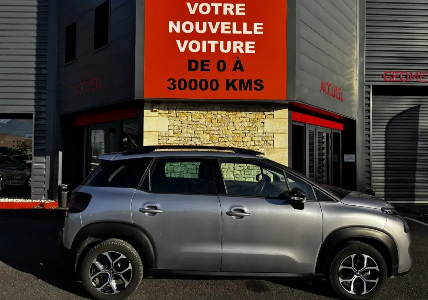 Profil côté gauche d'un Citroën C3 Aircross gris clair 2024 avec jantes alliage et barres de toit noires.