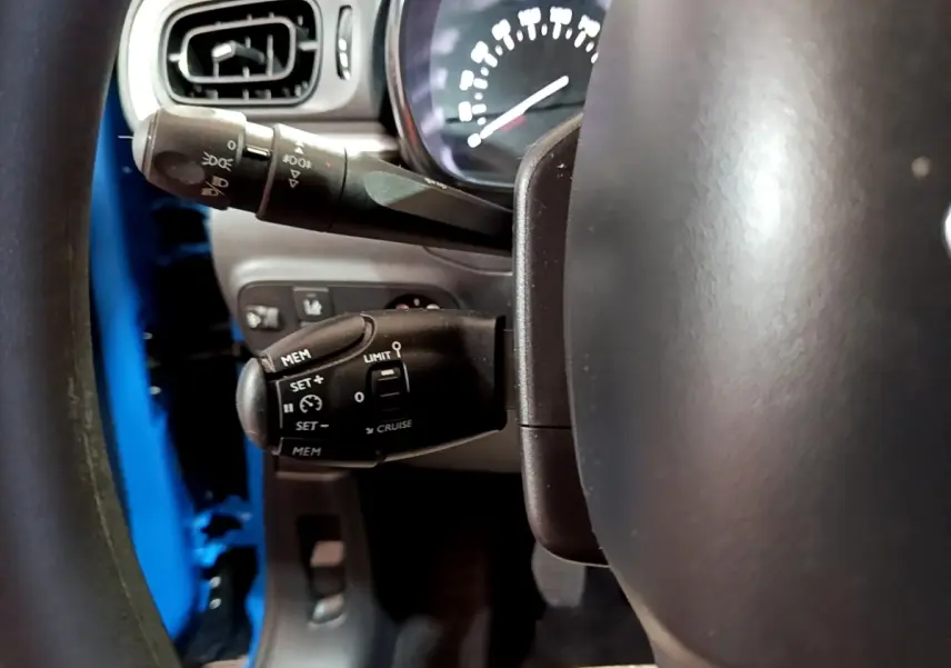 Gros plan sur le volant et les commandes de régulateur de vitesse d'une Citroën C3 bleu 2017, côté conducteur.