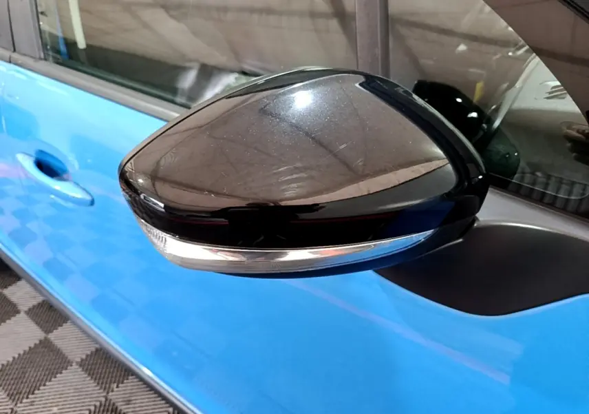Gros plan sur le rétroviseur noir avec clignotant intégré côté conducteur d'une Citroën C3 bleu vif.