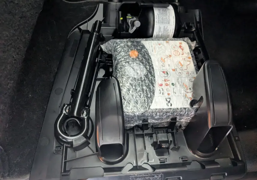 Vue rapprochée du compartiment de rangement sous le plancher arrière d’une Renault Twingo III gris Cassiopée, montrant le kit de réparation pneu.