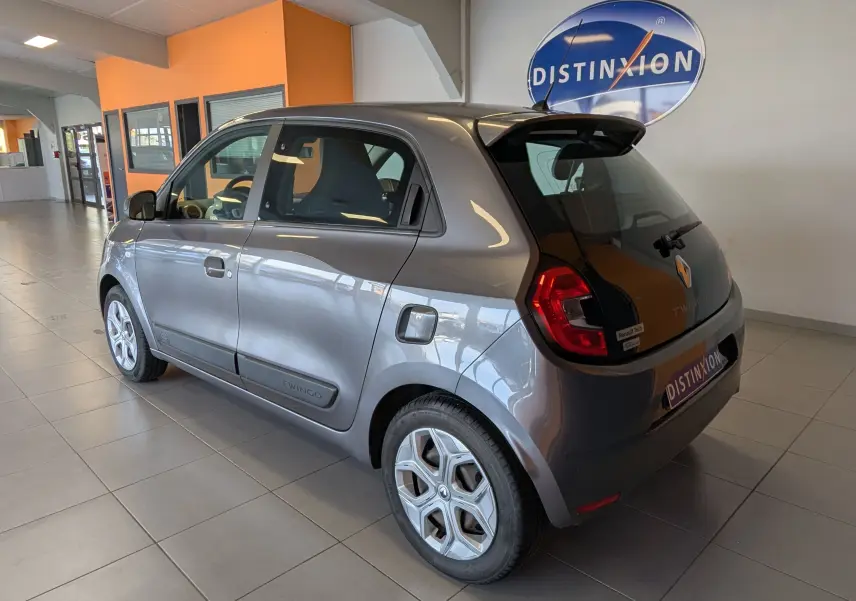 Vue 3/4 arrière droit d'une Renault Twingo III gris cassiopée en intérieur avec détails des feux et logo arrière visibles.