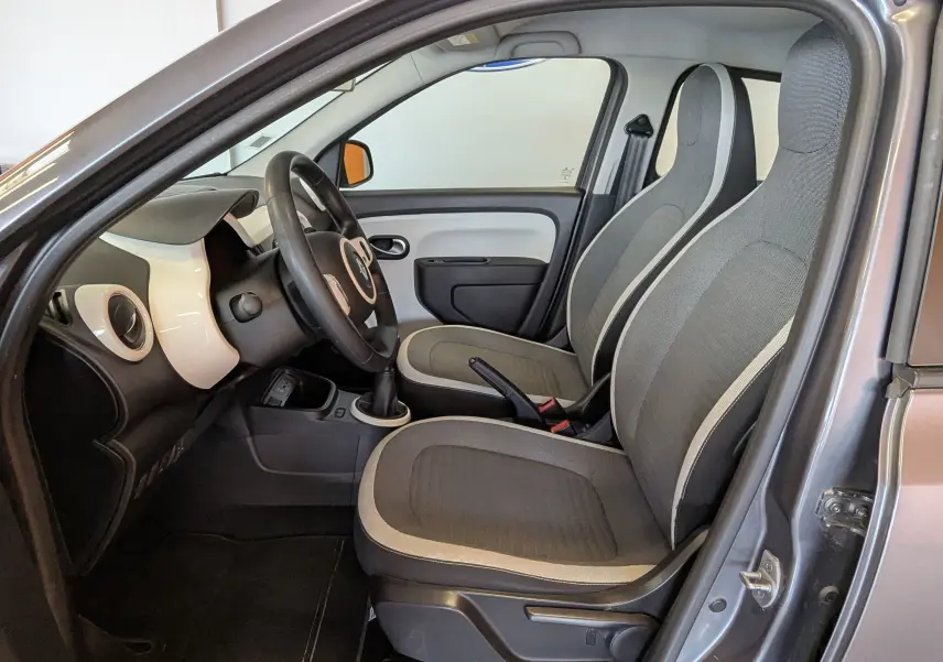 Vue intérieure côté gauche de la Renault Twingo III gris cassiopée, montrant les sièges avant et le tableau de bord clair.