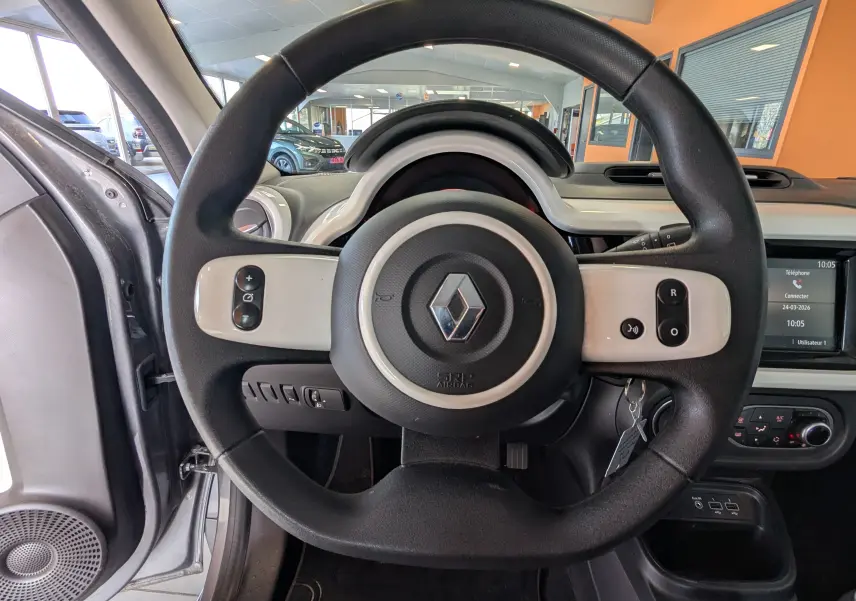 Vue intérieure centrée sur le volant noir et blanc de la Renault Twingo III gris Cassiopée, avec tableau de bord et écran tactile visibles.
