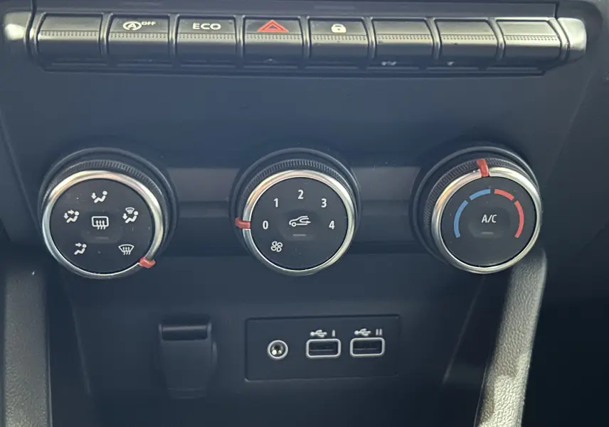 Gros plan sur les commandes de climatisation et les ports USB du tableau de bord d'une Renault Clio V noire.