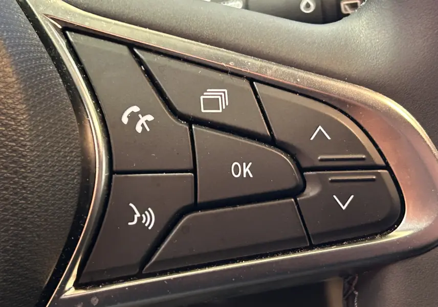 Gros plan sur les commandes noires du volant côté gauche de la Renault Clio V 2025, avec boutons de navigation et téléphone.