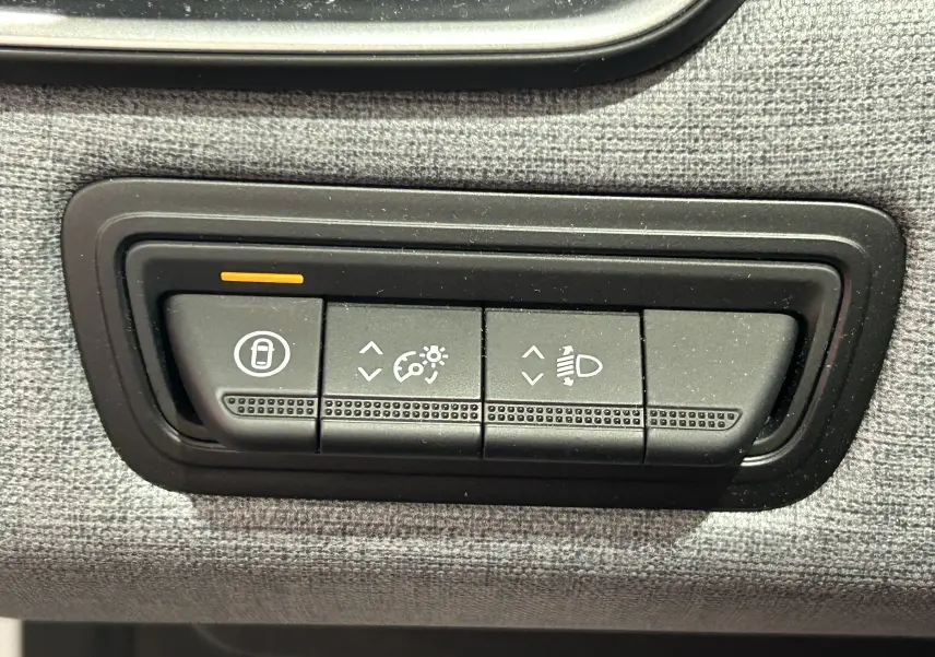 Gros plan sur les boutons de réglage d’éclairage et verrouillage intérieur dans une Renault Clio V noire, tableau de bord tissu gris.