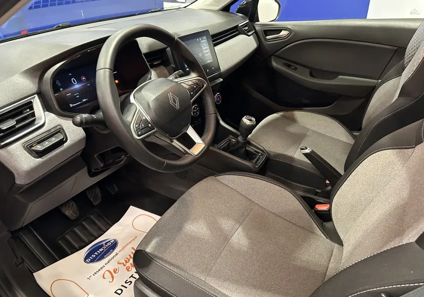 Intérieur avant droit de la Renault Clio V noire, montrant le volant, la console centrale avec boîte manuelle et les sièges tissu gris.