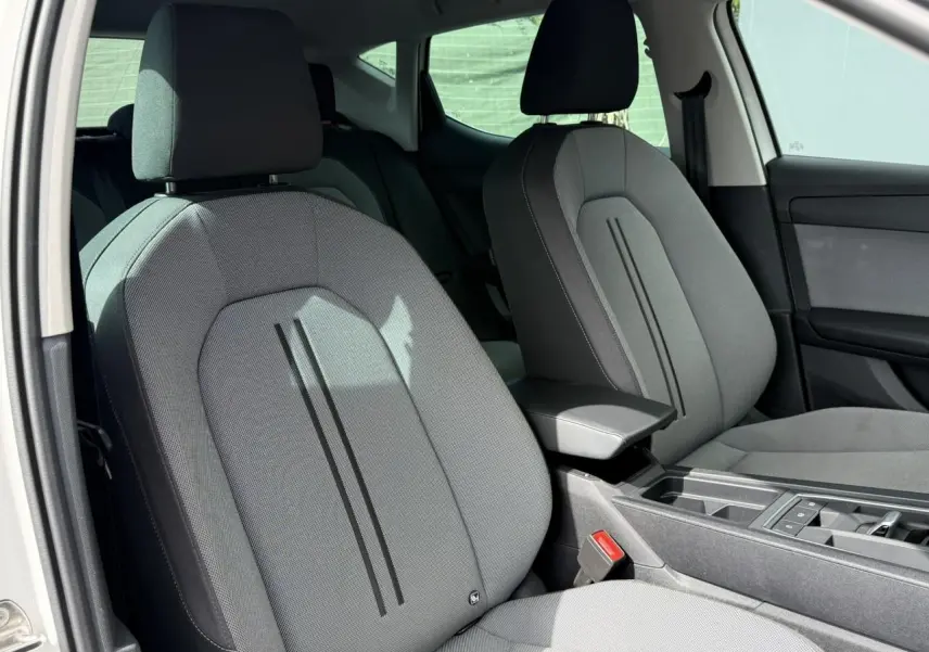 Vue intérieure côté conducteur du siège avant gris clair du SEAT LEON 2025 avec accoudoir central et console moderne.