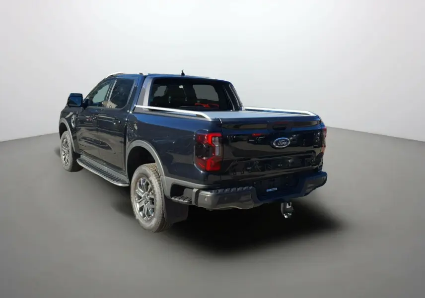 Ford Ranger noir agate en 3/4 arrière droit, double cabine avec barres de toit et attelage visible.