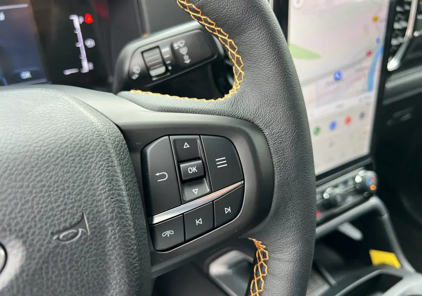 Gros plan sur la partie droite du volant du Ford Ranger Wildtrak Plus 2025, avec surpiqûres orange et écran tactile en arrière-plan.